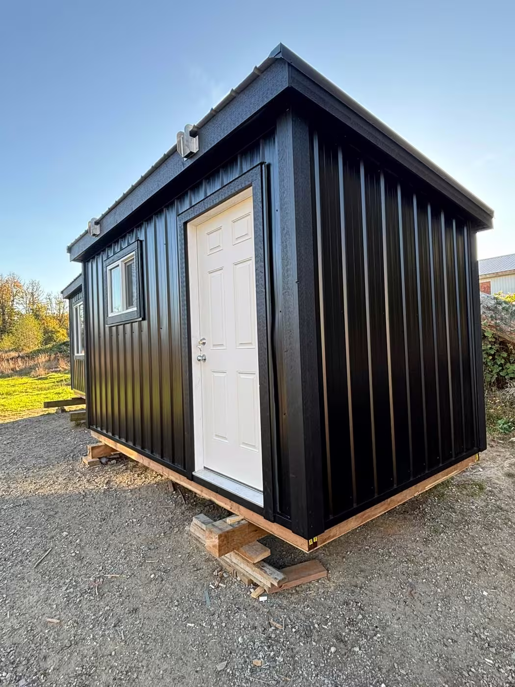 Black steel shed with a white six-panel door and a window, on timber blocks