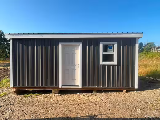 Long charcoal steel shed with white trim, a white door and a window, on timber skids