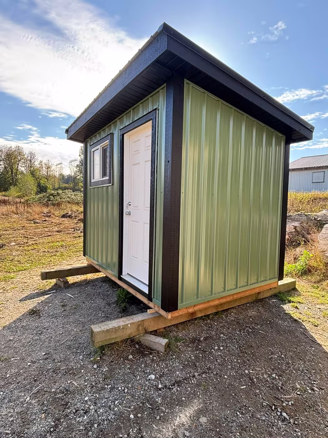 Green steel shed with black trim and a white door, on timber skids