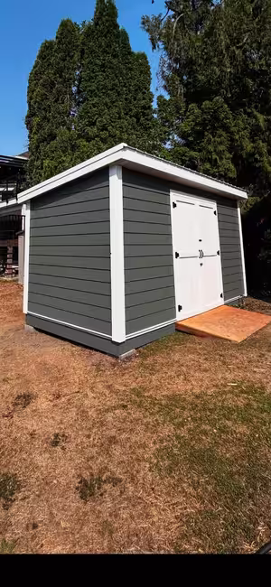 Grey-sided shed with white trim, white double doors and a plywood ramp, on dry grass