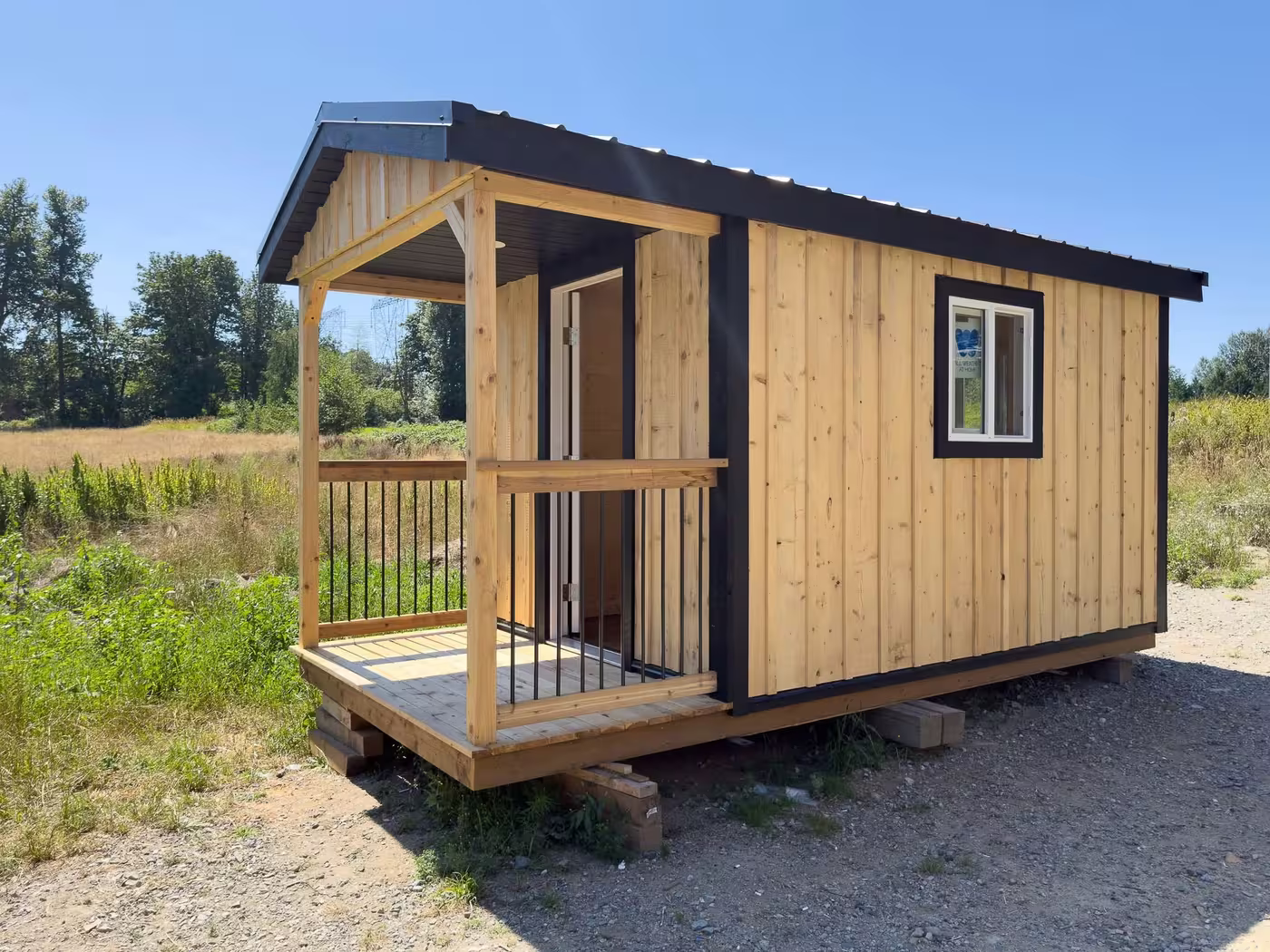 Cedar-stained cabin with a covered front porch and railing, black trim and a window
