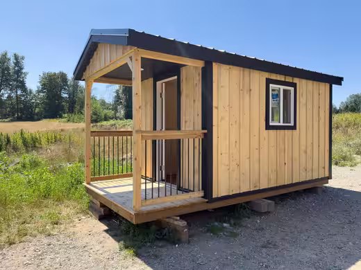 Cedar-stained cabin with a covered front porch and railing, black trim and a window