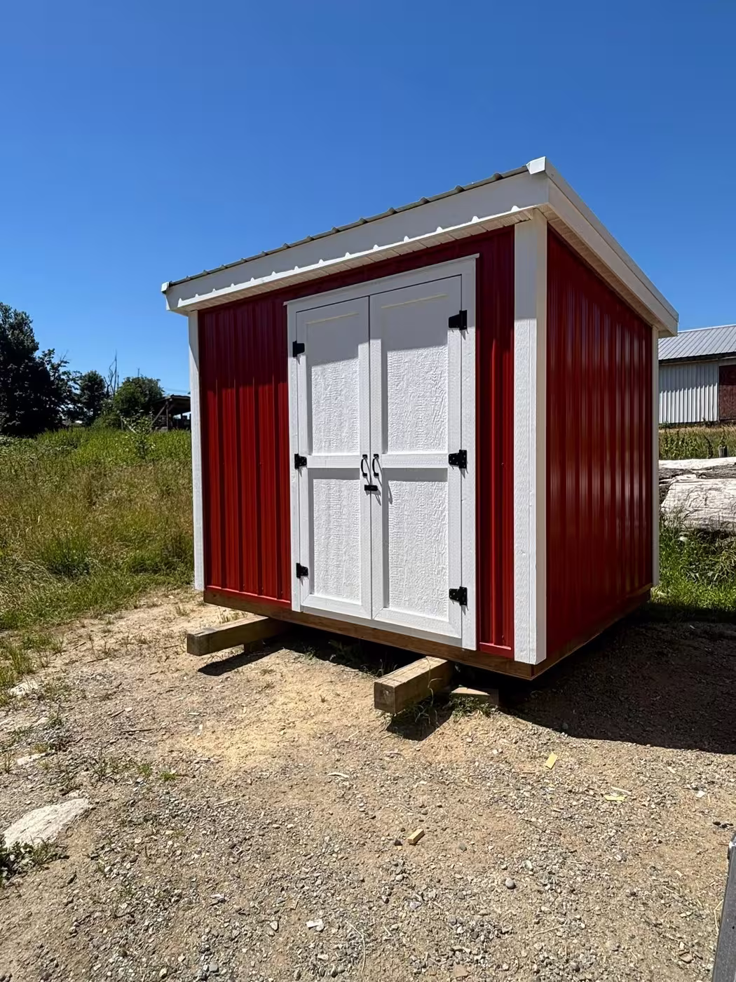 Red steel shed with white trim and white double doors, on timber skids